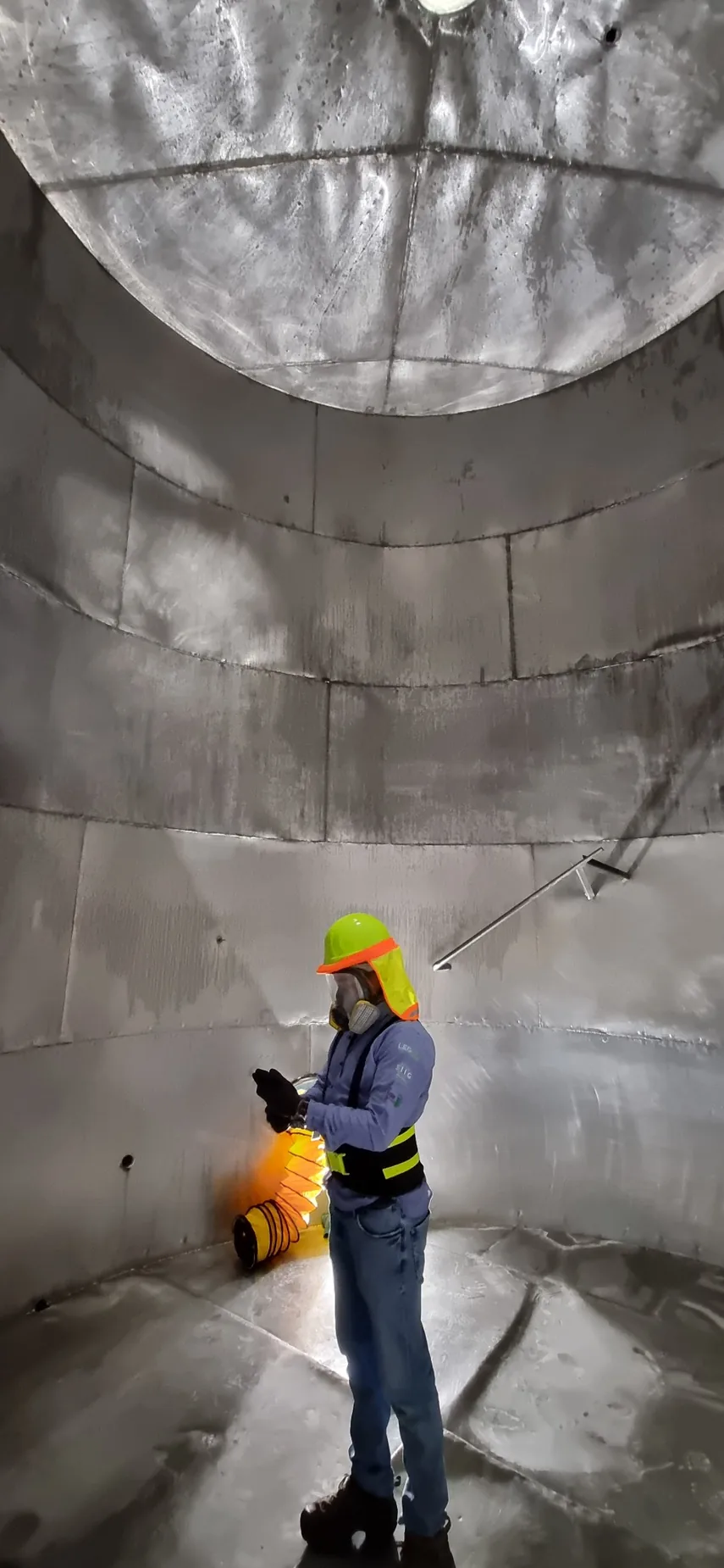 Trabajador de LEGOS dentro de un tanque metálico vertical observando su interior