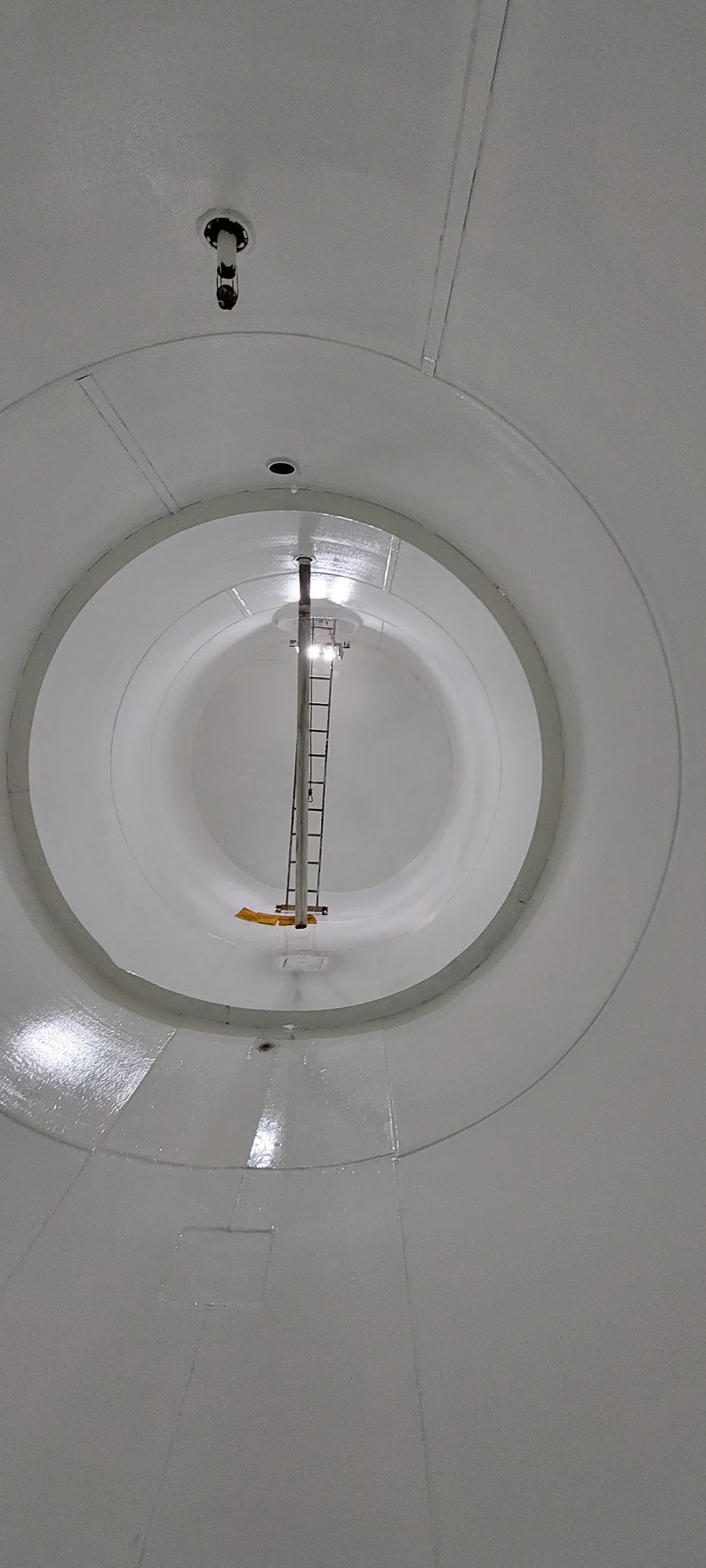 Interior blanco de un tanque con escalera y tubería vertical.